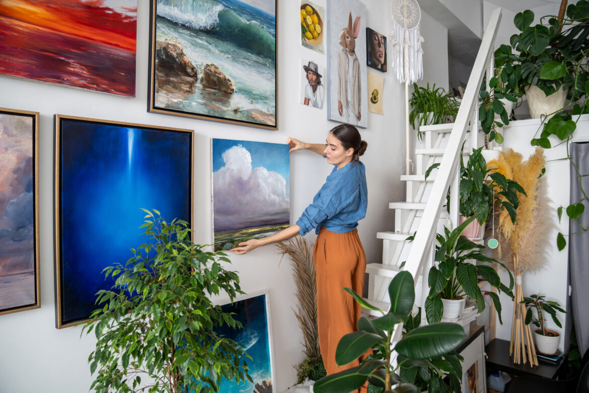 focused woman artist hanging paintings wall creative art home studio workshop apartment