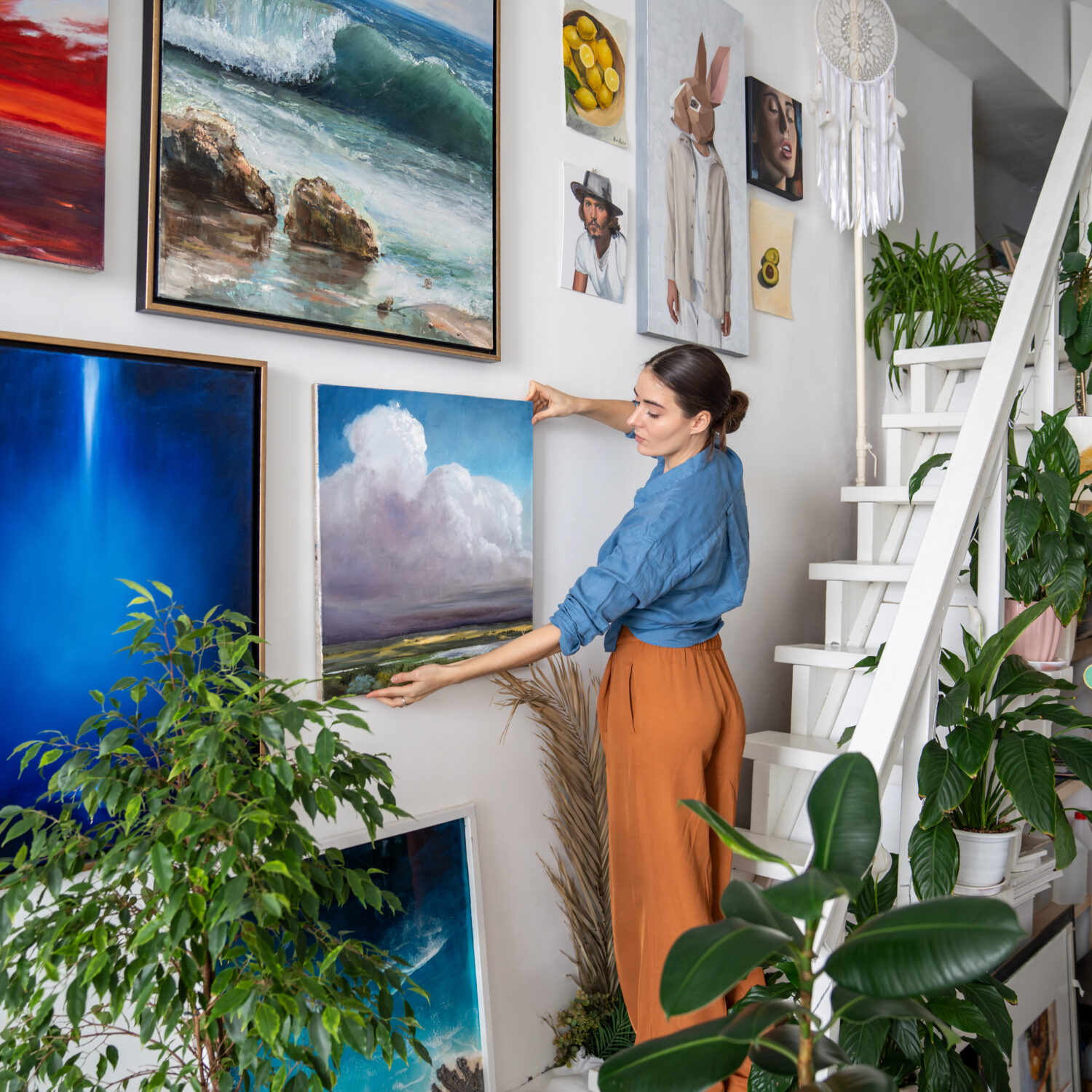focused woman artist hanging paintings wall creative art home studio workshop apartment